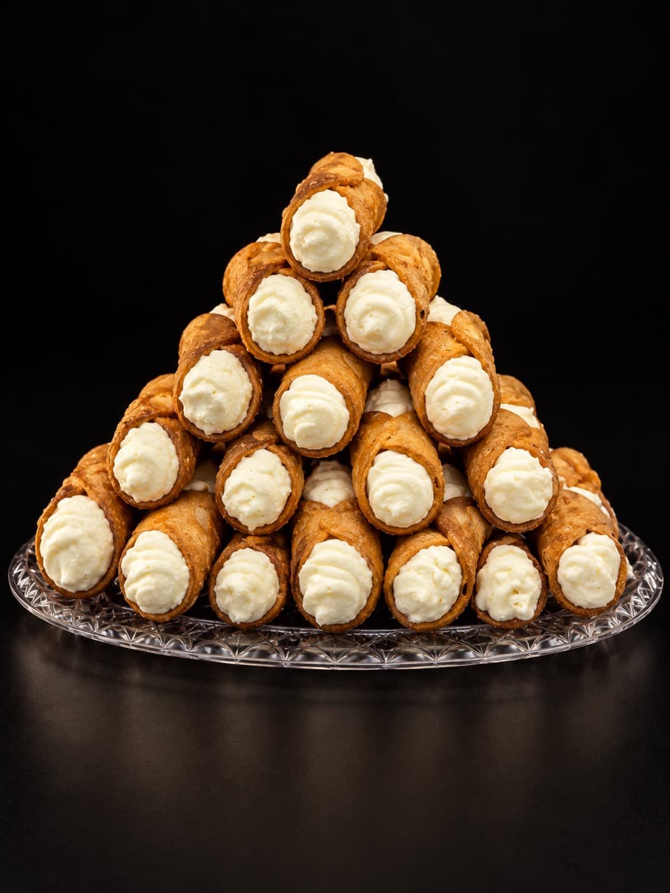 A stack of cream-filled Sicilian cannoli on a glass platter