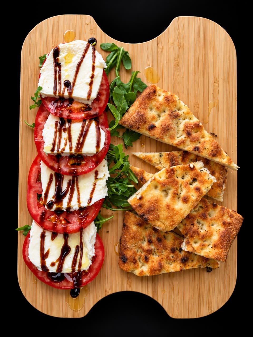 Tri Colore salad with tomatoes, fresh mozzarella, arugula, and balsamic glaze on a wooden board